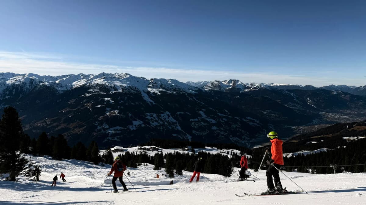 Skiløpere i en solfylt alpinbakke med fjell i bakgrunnen