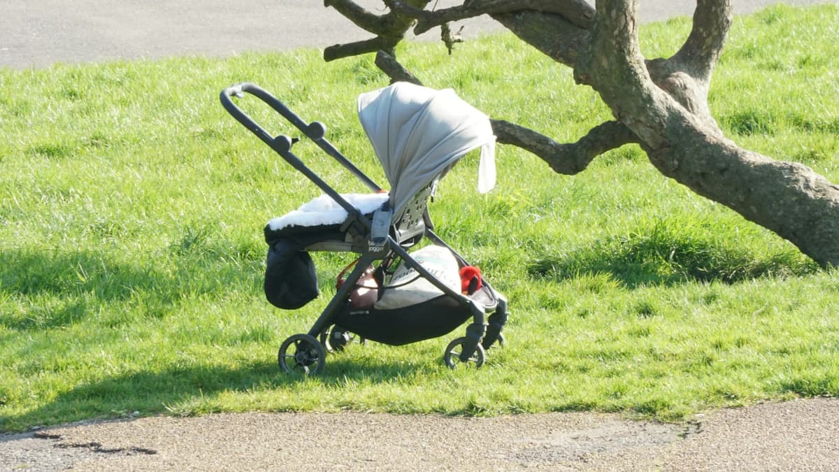 Barnevogn parkert på gresset under et tre