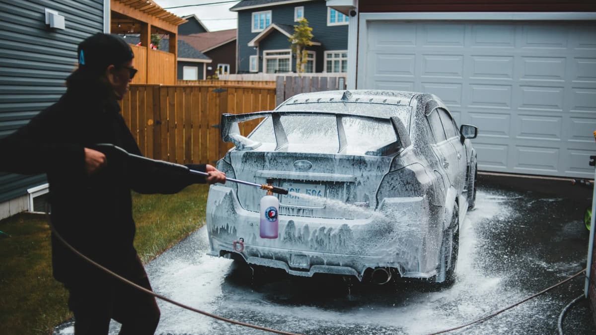 Person som vasker en skumdekket bil med høytrykkspyler i oppkjørselen