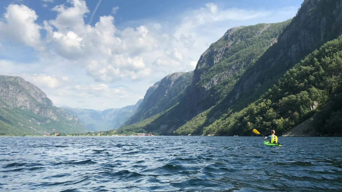 Padler i grønn kajakk på en fjord med bratte fjellsider