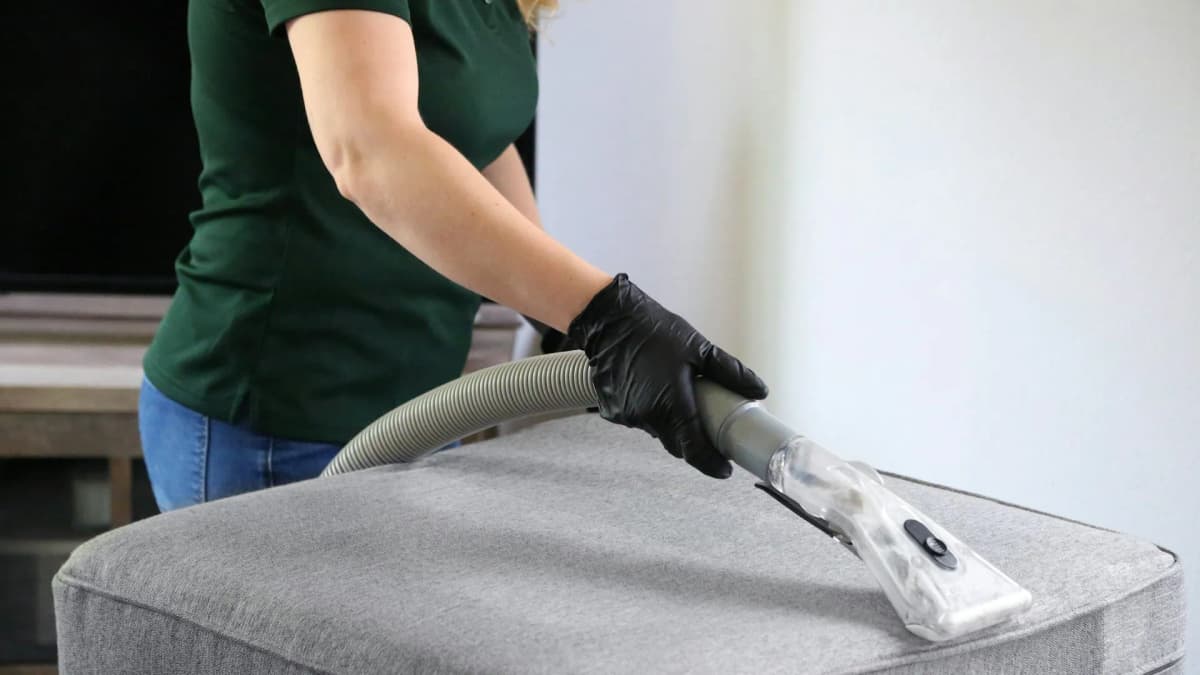 Person med hansker som renser en grå puff med munnstykket på en tepperenser